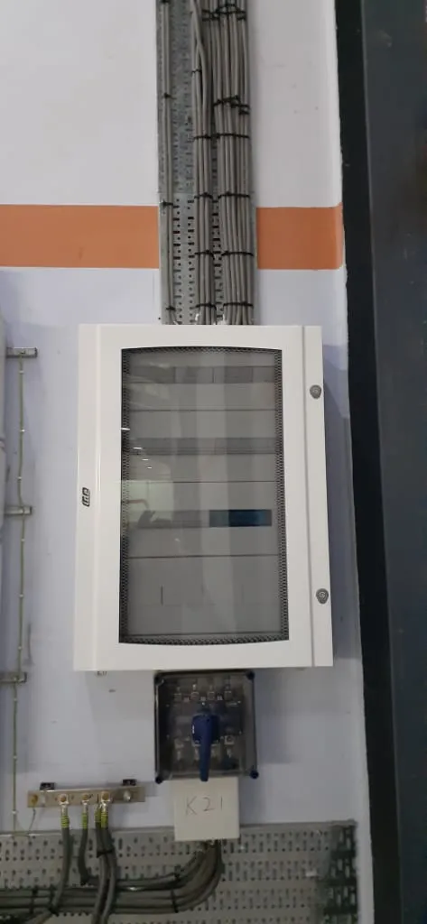 Groepenkast K21 aan de wand, met een hoofdschakelaar eronder en kabels via de kabelgoot